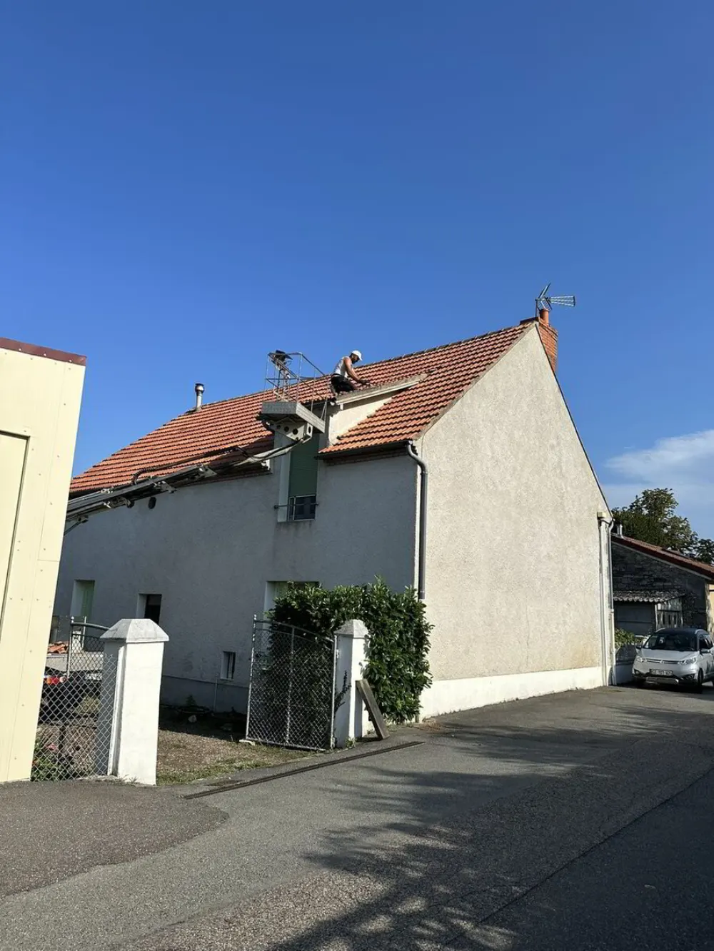 Un artisan dans la nacelle d'un camion-grue travaillant sur les tuiles de rive d'une maison.
