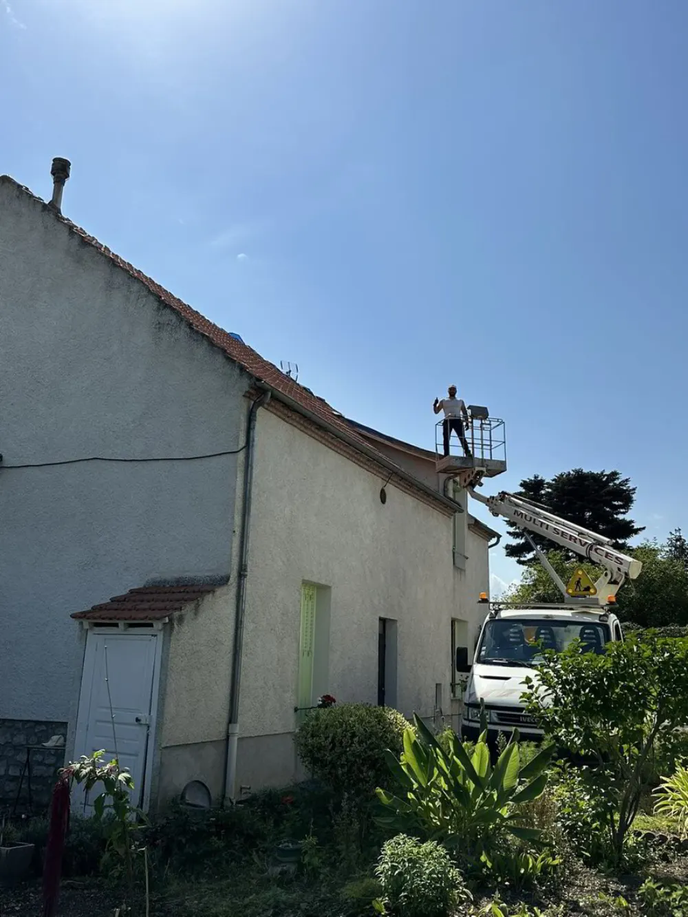 Artisan debout dans une nacelle élévatrice près du bord du toit d'une maison.