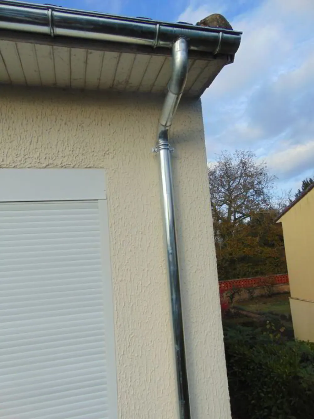 Tuyau de descente de gouttière en zinc neuf fixé sur une façade en crépi beige.