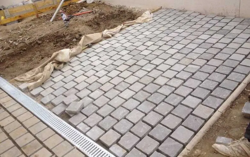 Pose de pavés gris de forme carrée avec caniveau d'évacuation métallique intégré pour une allée.