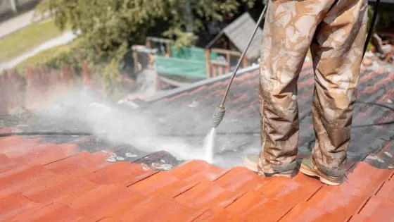 Gros plan sur les jambes d'un ouvrier nettoyant des tuiles rouges au jet haute pression.