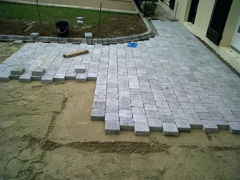 Pose de pavés gris rectangulaires sur un lit de sable pour une allée ou terrasse.