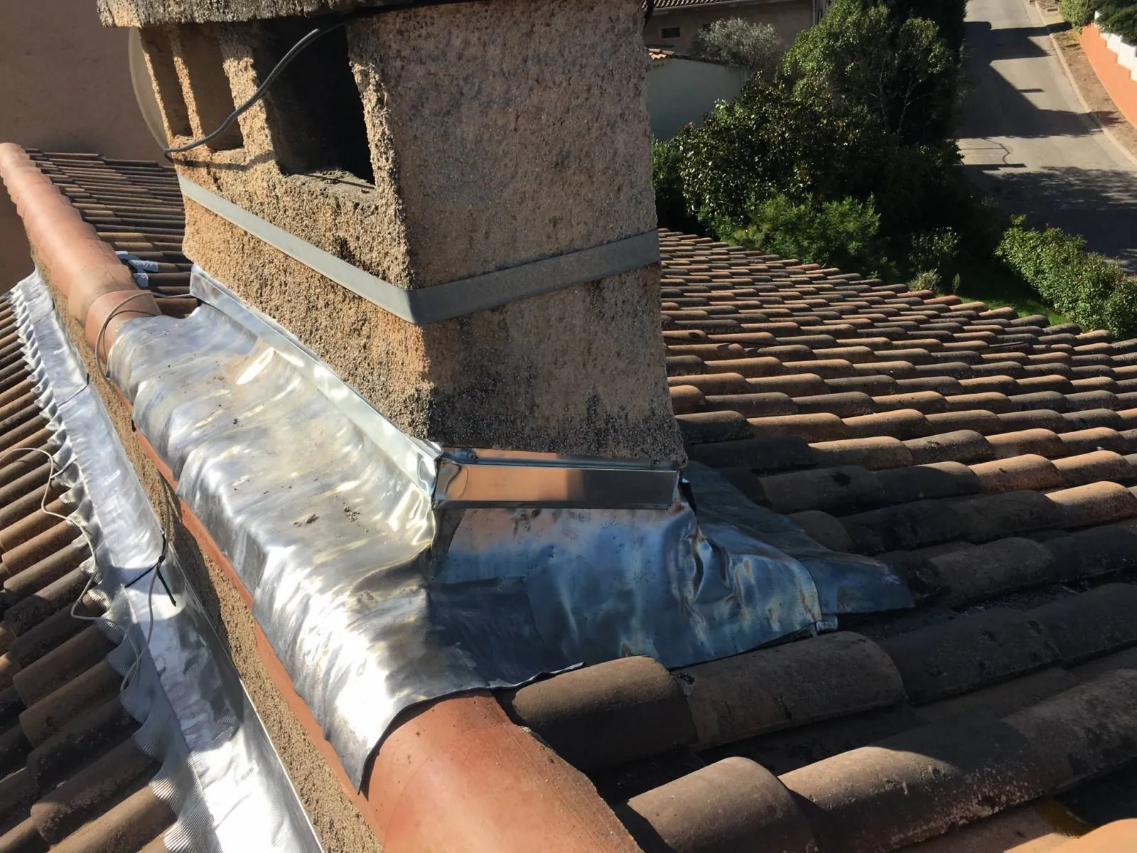 Solin en plomb et zinc refait à neuf à la base d'une souche de cheminée carrée en crépi sur un toit en tuiles.
