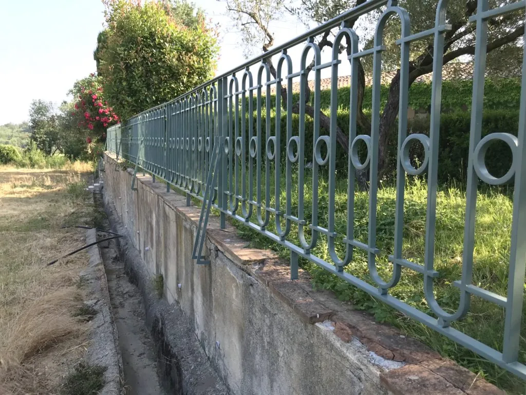 Grille de clôture métallique verte fraîchement peinte et installée sur un muret en béton.