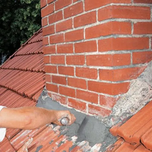 Ouvrier appliquant à la truelle un mortier d'étanchéité au pied d'une cheminée en briques.