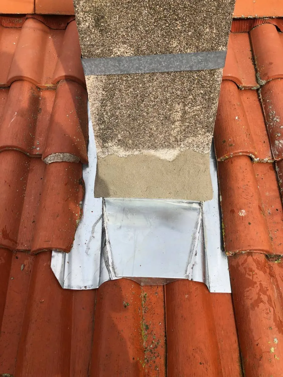 Bande d'étanchéité métallique et bande de plomb marouflée à l'avant d'une souche de cheminée en crépi gris.