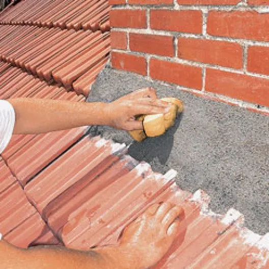 Lissage à l'éponge d'un solin en ciment faisant la jonction entre le mur en brique et les tuiles du toit.