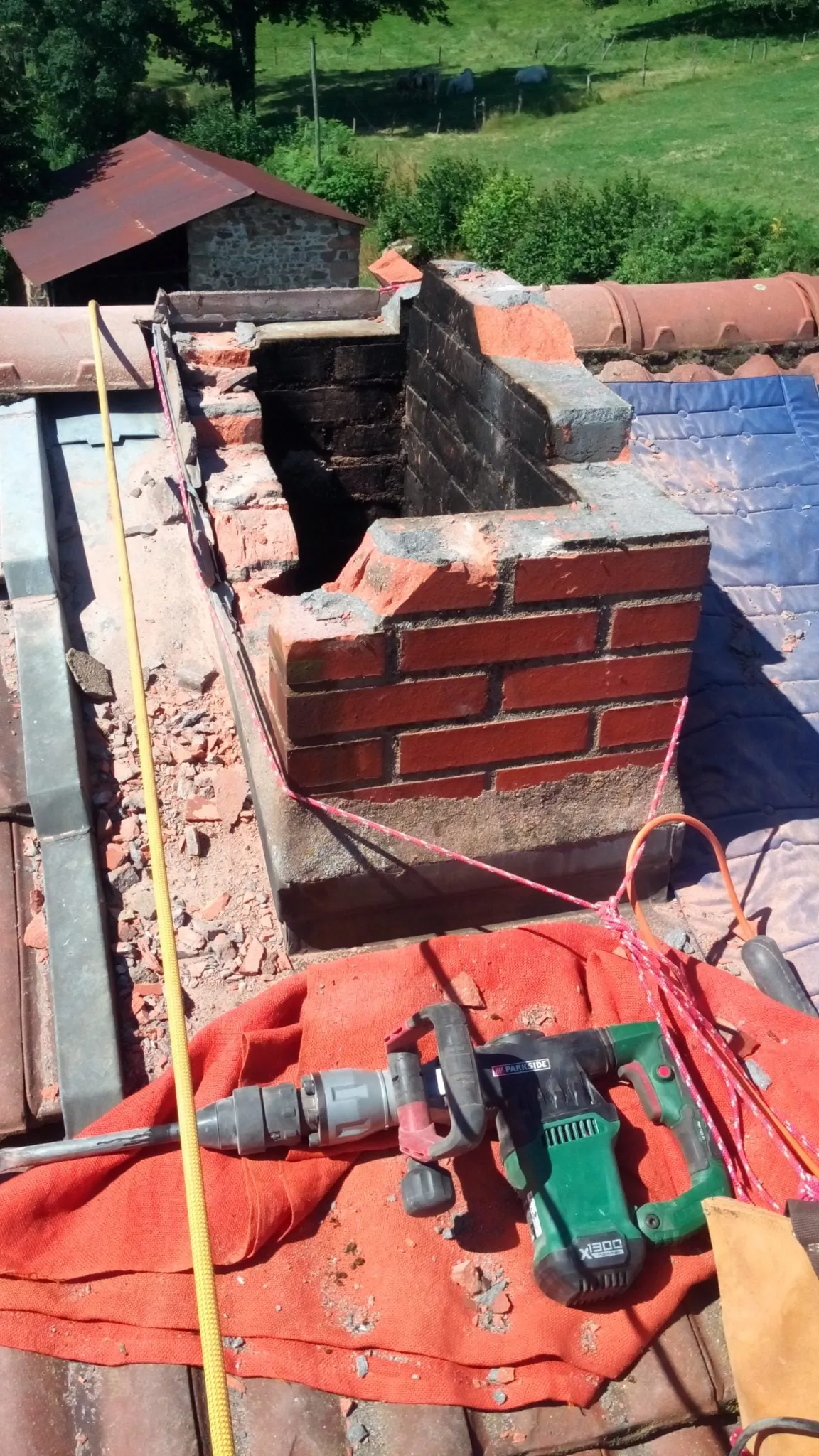 Vue en plongée d'une cheminée en brique en cours de démolition avec un marteau-piqueur posé à côté.