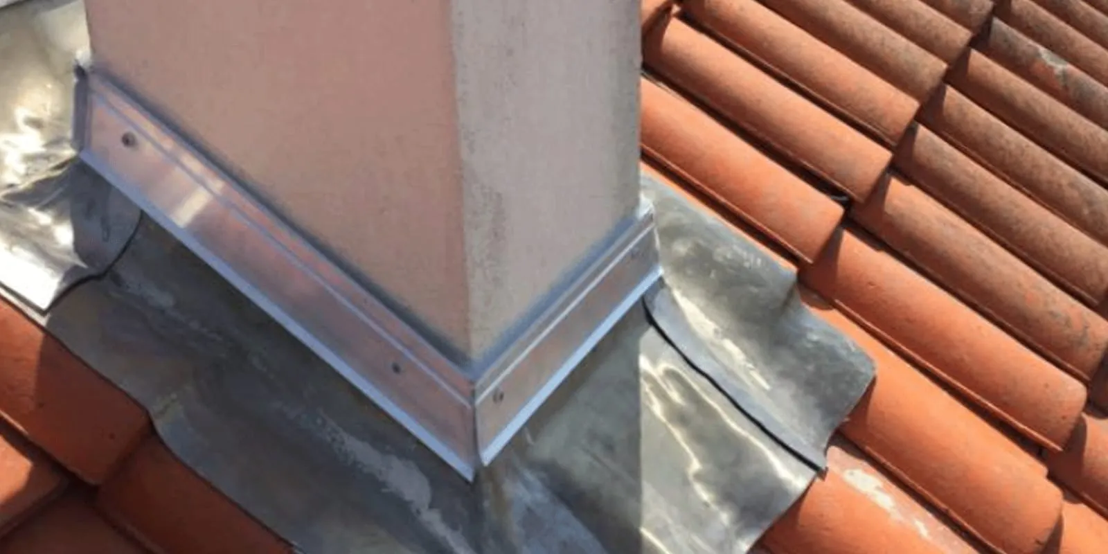 Détail d'un solin à bavette plomb et profilé en zinc fixé par des vis à la base d'une cheminée refaite à neuf.