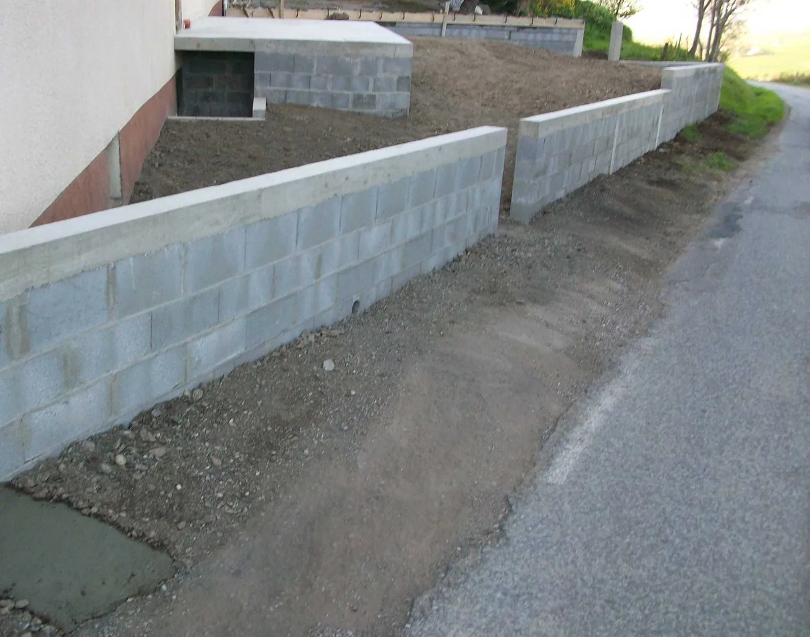 Construction d'un muret de soutènement en parpaings bruts le long d'une route en pente.